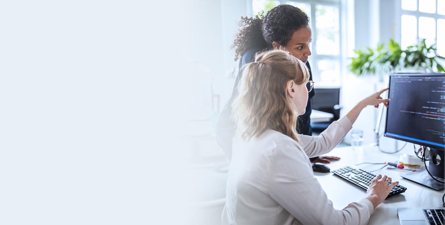 Two business women looking at a desktop monitor utilizing Viasat managed wifi solutions